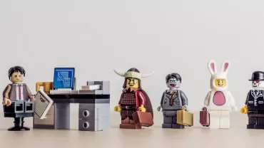 Lego figures in costumes wait in line by a small office desk.