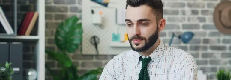 Person in an office setting with a brick wall and plants in the background.