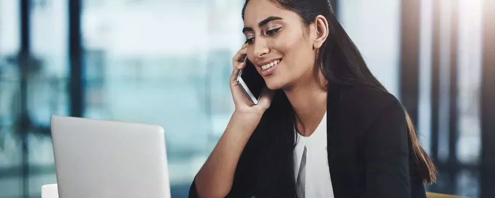 Person smiling while on a phone call, sitting at a desk with a laptop.